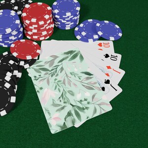 May include: Poker chips in black, red, and blue are stacked on a green felt surface. A deck of playing cards with a floral design is fanned out, with the ten of hearts, diamonds, and spades visible.