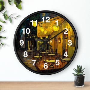 May include: A round wall clock with a black frame. The clock face features a painting of a cafe scene at night, with yellow lights and tables. The clock hands are black, and the numbers are white.