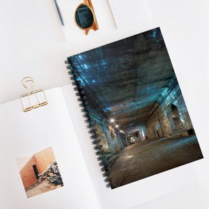 May include: Spiral-bound notebook featuring a digitally enhanced image of a long, dark tunnel with arched doorways and overhead lighting. The image has a blue and gray color scheme. The notebook is open on a white surface with a gold paper clip and sunglasses.
