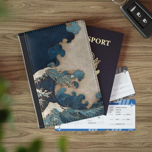 May include: A passport cover with a navy blue and white wave design, a passport, and two boarding passes are on a wooden surface. The passport cover features a black border and a Japanese-inspired wave pattern. A car key is also visible.