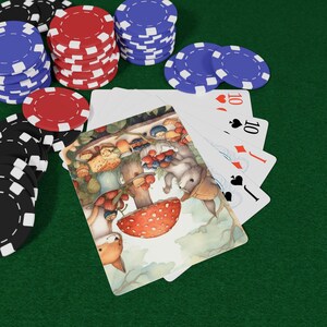 May include: A deck of playing cards fanned out on a green surface, with the top card featuring an illustration of a fox and a squirrel near a red mushroom with white spots. Stacks of red, blue, and black poker chips surround the playing cards.