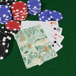 May include: A hand of playing cards fanned out with a light green floral and botanical pattern on the back, accompanied by stacks of red, blue, and black poker chips. The cards display standard suits and numbers including a ten and a jack.