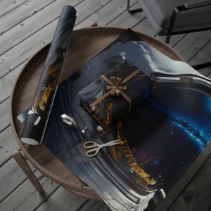 May include: A roll of wrapping paper and a rectangular gift box wrapped in the same paper, both featuring a detailed space-themed print of an astronaut helmet with a gold visor reflecting a nebula. A pair of silver scissors and tape are included.
