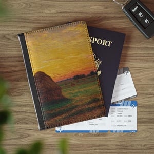 Può includere: Una copertina per passaporto con un dipinto di un paesaggio di un tramonto su un campo con covoni di fieno. Un passaporto blu scuro e due carte d'imbarco sono accanto. È visibile anche una chiave dell'auto.