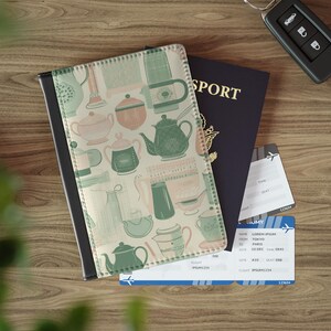 Pode incluir: Uma capa de passaporte com dorso preto e frente creme com um padrão de bules verdes e pêssego. Um passaporte azul escuro, bilhetes de avião e uma chave de carro também são visíveis.