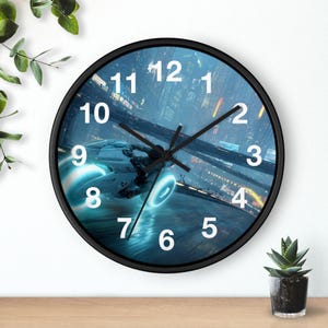 Puede incluir: Un reloj de pared redondo con marco negro y una esfera que muestra una escena futurista de una persona montando una motocicleta luminosa a través de una ciudad oscura. El reloj tiene números blancos grandes del 1 al 12 y manecillas negras.