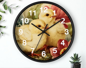 May include: A round wall clock with a black frame. The clock face features two yellow chicks with a floral background of red and green. White numerals mark the hours, and black hands indicate the time.