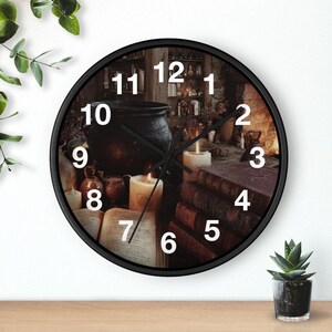 May include: Black circular wall clock with a witchy theme. The clock face depicts a cauldron, candles, books, and a cosy fireplace scene. The clock hands are black, and the numbers are white.