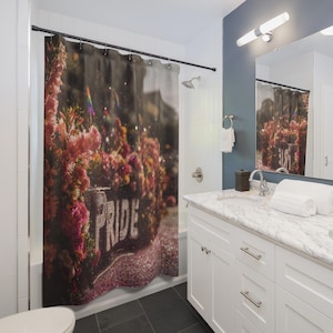 Può includere: Una tenda da doccia con un design floreale e la parola "PRIDE" a lettere bianche. La tenda presenta fiori rosa e rossi con un effetto glitterato, creando un'atmosfera vibrante e festosa. L'ambiente bagno comprende un mobile bianco e uno specchio.