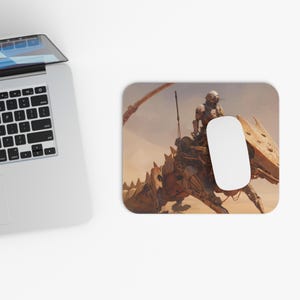May include: A rectangular mousepad featuring a detailed illustration of a mechanical creature ridden by a figure in a helmet, set against a desert backdrop. A white computer mouse rests on the pad.