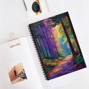 May include: Spiral-bound notebook featuring a vibrant forest scene with a path winding through colorful trees. The artwork showcases a palette of purple, green, yellow, and orange hues. The notebook is open on a white surface, with a gold paper clip and sunglasses nearby.
