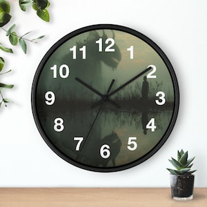 Puede incluir: Un reloj de pared redondo con marco negro y números blancos. La esfera presenta una ilustración de un paisaje oscuro y brumoso con la silueta de una gran criatura y una persona cerca del agua, con un reflejo visible en la parte inferior.