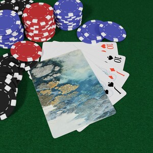 May include: Poker chips in red, blue, and black are stacked on a green felt surface. Playing cards with the number 10 are fanned out. One card has a blue and gold abstract design.