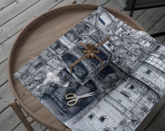 May include: A wrapped gift with a brown ribbon and bow sits on a sheet of wrapping paper with a black and white architectural design. Gold scissors and a roll of white ribbon are also on the paper, which is on a wooden table.