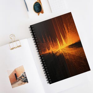 May include: A spiral-bound notebook with an abstract design. The cover displays a dark, textured background with a bright orange and yellow gradient, reminiscent of a sunset or fiery landscape. The notebook is open on a white surface.