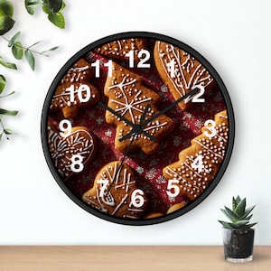May include: A round wall clock with a black frame featuring a design of gingerbread biscuits. The clock face displays various biscuit shapes, including trees and hearts, with white icing details and white numbers.
