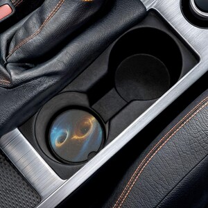 Peut inclure: Un porte-gobelet de voiture avec un dessous de verre présentant un motif abstrait bleu et or. Le dessous de verre est placé dans le porte-gobelet, entouré de cuir noir et d'une garniture argentée.