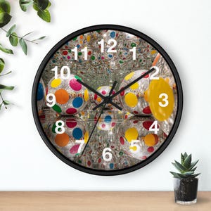 May include: A round wall clock with a black frame. The clock face features a mirrored background with colorful polka-dotted spheres. Black clock hands point to the time. Numbers 1 through 12 are displayed in white.