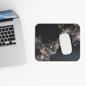 May include: A black rectangular mousepad with a white wireless mouse. The mousepad features a geometric design with gold and white accents. A silver laptop is partially visible in the image.