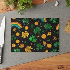 May include: Rectangular cutting board with a black background featuring a pattern of gold coins, green shamrocks, yellow flowers, and rainbows. The board is made of a durable material and is suitable for food preparation.