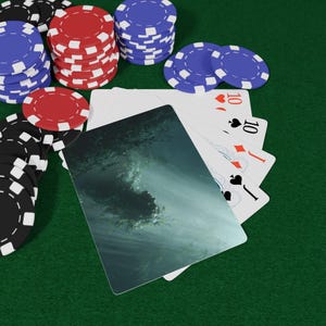 May include: Poker set on a green felt surface. Stacks of red, blue, and black poker chips surround a hand of playing cards, including a card with a wave design and three cards showing the number 10.