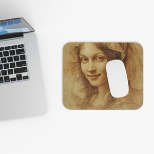 May include: A rectangular mouse mat with a sepia-toned sketch of a woman's portrait. A white computer mouse is positioned on the right side of the mat. The woman has long hair and is wearing a head covering.