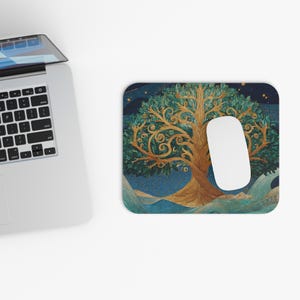 May include: A rectangular mousepad featuring a detailed illustration of a golden tree with green leaves against a dark blue background. A white computer mouse rests on the pad. The design includes swirling patterns and a starry sky.