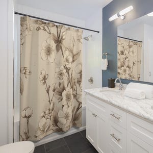 May include: A beige shower curtain with a sepia floral pattern. The curtain displays detailed drawings of flowers and leaves, giving a vintage botanical feel. The curtain is in a bathroom with white fixtures and dark grey floor tiles.