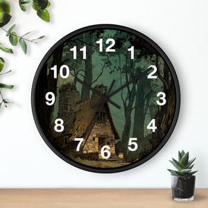 May include: A round wall clock with a black frame. The clock face features a forest scene with a small cottage and large trees. White numerals mark the hours. The clock hands are black.
