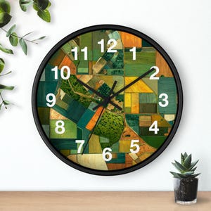 May include: A round wall clock with a black frame and a face featuring an aerial view of agricultural fields in shades of green, yellow, and orange. The clock has white numbers from 1 to 12 and black hour, minute, and second hands.