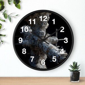 May include: Black wall clock featuring a detailed illustration of a space station against a black background. The clock has white numerals and black hands. The clock's design is a unique blend of science fiction and timekeeping.