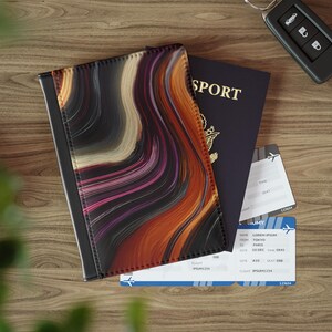 May include: A passport holder with a swirling abstract design in shades of orange, purple, and black. A dark blue passport and two boarding passes are visible. A car key is also present on the wooden surface.