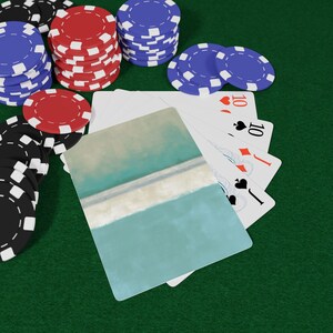 May include: Stacks of red, black, and blue poker chips are arranged on a green surface, with playing cards and a decorative card featuring a teal and white abstract design. The playing cards show the number 10 in the suits of hearts, spades, and diamonds.