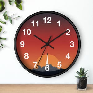 Könnte beinhalten: Eine runde, schwarze Wanduhr mit einem Zifferblatt im Sonnenuntergangs-Design. Das Zifferblatt zeigt einen Farbverlauf von Orange und Rot, mit einer Silhouette eines Raketenstarts. Weiße Ziffern markieren die Stunden.