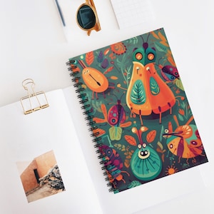 May include: A spiral-bound notebook with a colorful insect and floral design on the cover. The cover features a teal background with orange, teal, and purple insects and flowers. The notebook is open on a white surface.