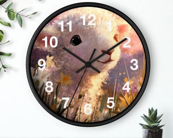 May include: A round wall clock with a black frame. The clock face features a painting of a white lamb in a field of flowers. The clock hands are black, and the numbers are white.