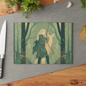 Könnte beinhalten: Ein rechteckiges Glasschneidebrett mit einer grünen und beigen Illustration einer Person mit langem Haar, die eine Krone trägt und Pfeil und Bogen hält, während sie in einem Wald neben einem Hirsch steht. Das Design nutzt Salbei- und Dunkelgrüntöne.