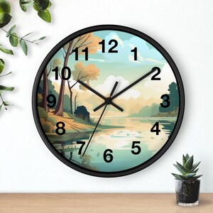 Puede incluir: Un reloj de pared redondo con marco negro. La esfera del reloj presenta una serena pintura de paisaje de un lago y árboles. Las manecillas negras indican la hora. Los números están en una fuente negra y fácil de leer.