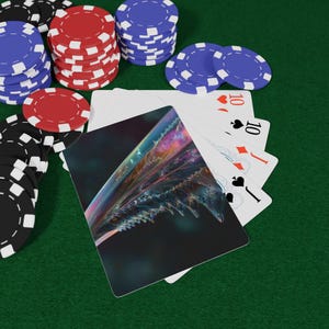 以下が含まれることがあります： ポーカーゲームのシーン。トランプと赤、黒、青のポーカーチップの山。カードには数字の10とカラフルな抽象的なデザインが描かれています。背景は緑色のフェルトの表面です。