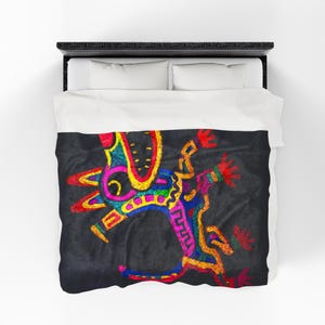 May include: A black bedspread with a colorful, abstract design. The design features a central figure with red, yellow, blue, and pink accents. The bedspread is on a black bed frame with white pillows.