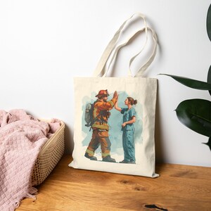May include: A beige canvas tote bag featuring a watercolor illustration of a firefighter and a nurse giving each other a high five. The firefighter is wearing orange protective gear, and the nurse is in blue scrubs. The background has a light blue wash.