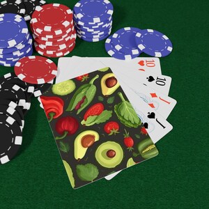 May include: A hand of playing cards featuring a vegetable pattern with avocados, tomatoes, and peppers, fanned out alongside stacks of red, blue, and black poker chips. The cards display standard suit symbols including hearts, spades, and diamonds.