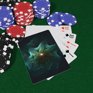 Könnte beinhalten: Ein Kartenspiel mit einem Nebel-Design auf der Rückseite, das ein leuchtendes Zentrum und türkisfarbene Wolken zeigt, aufgefächert neben Stapeln von roten, blauen und schwarzen Pokerchips auf einer grünen Filzoberfläche. Die Karten zeigen Herz- und Pik-Zehn.