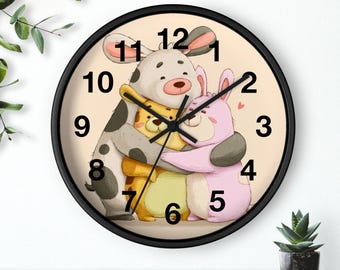 May include: A round wall clock with a black frame. The clock face features a cartoon illustration of three hugging animals: a dog, a bear, and a rabbit. The clock hands point to 12:00. The background is a light beige color.