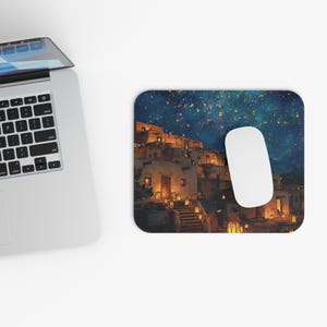 May include: Mousepad featuring a nighttime village scene with warm-toned buildings and a starry sky. A white computer mouse rests on the pad. The design evokes a sense of tranquility and wonder, perfect for a home office or workspace.