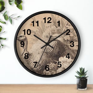 May include: A round wall clock with a black frame. The clock face features a sepia-toned illustration of a turkey surrounded by floral elements. Black hands indicate the time. The numbers are in a classic font.