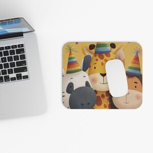 Puede incluir: Alfombrilla de ratón rectangular con una ilustración caprichosa de una cebra, una jirafa y un personaje de piel morena, todos con sombreros de fiesta coloridos. Un ratón de ordenador blanco descansa sobre la alfombrilla. El fondo es de color amarillo claro.