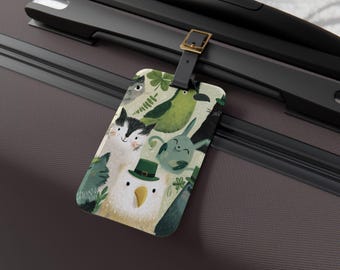 May include: A luggage tag featuring a whimsical illustration of various animals, including cats, a rabbit, and a bird wearing a green hat. The tag has a black strap with a gold-colored buckle, and is attached to a dark gray suitcase.