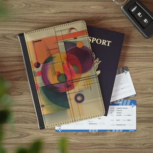 May include: A passport cover with an abstract design in orange, purple, and green, next to a navy blue passport and two airline tickets. A car key is also visible. The passport cover has a black border.