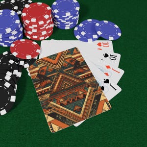 Könnte beinhalten: Ein Pokerspiel-Setup mit Spielkarten und Pokerchips. Die Karten zeigen ein geometrisches Muster in Orange, Türkis und Braun. Stapel von roten, blauen und schwarz-weißen Chips sind auf einer grünen Filzoberfläche zu sehen.